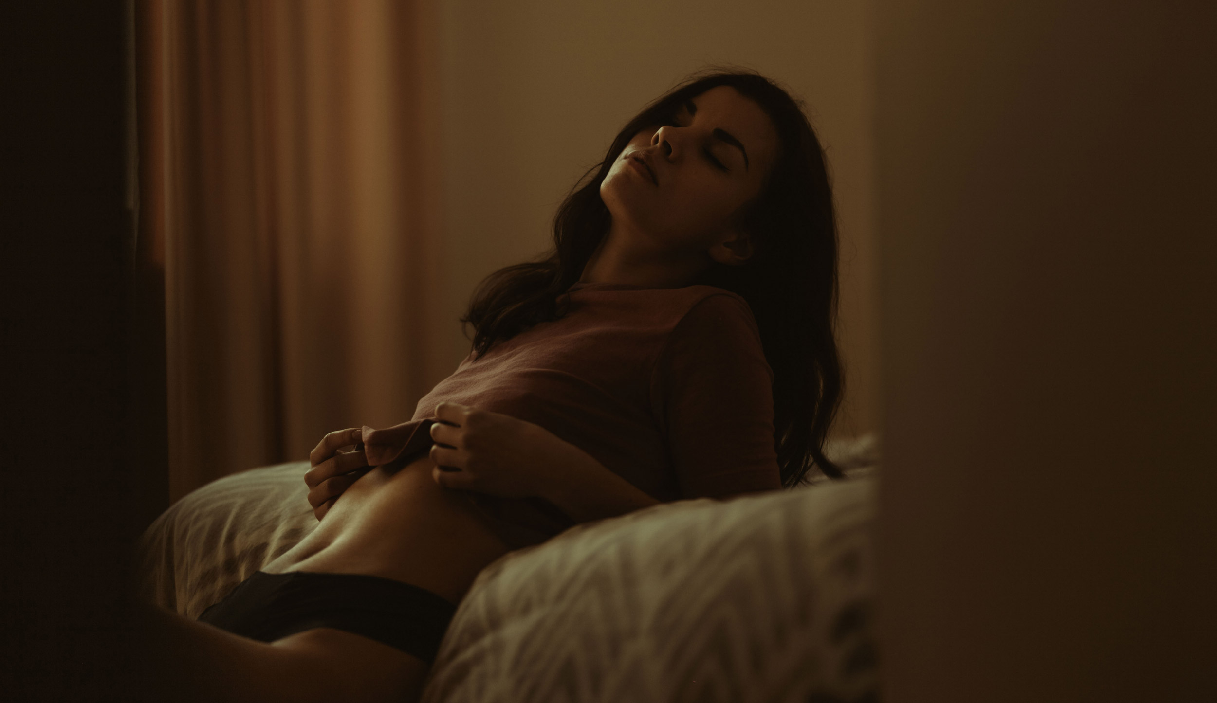 Photo boudoir à l'éclairage naturel d'une femme aux yeux fermés sur le bord de son lit